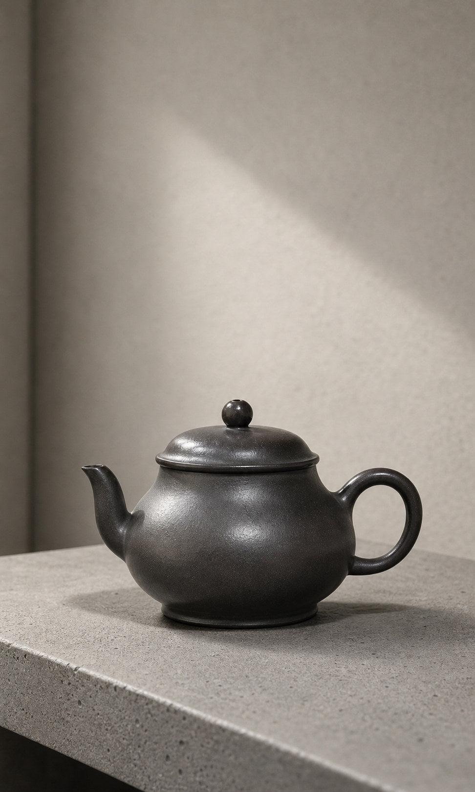 Black Hei Duntou Pan Hu teapot displayed on pale stone