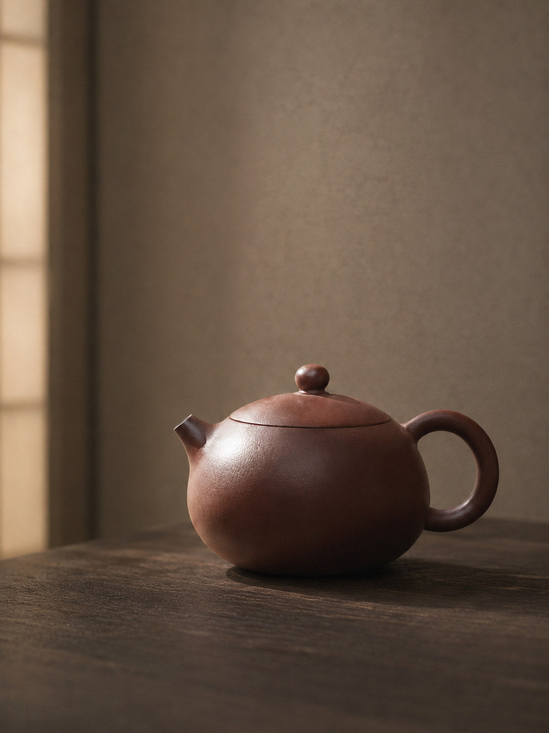 Xishi teapot, wide alternate side view on a dark table in soft window light