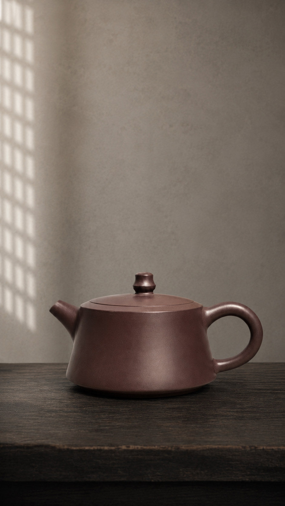 Zhu Chu teapot, wide front-side view on a dark tabletop with lattice shadows